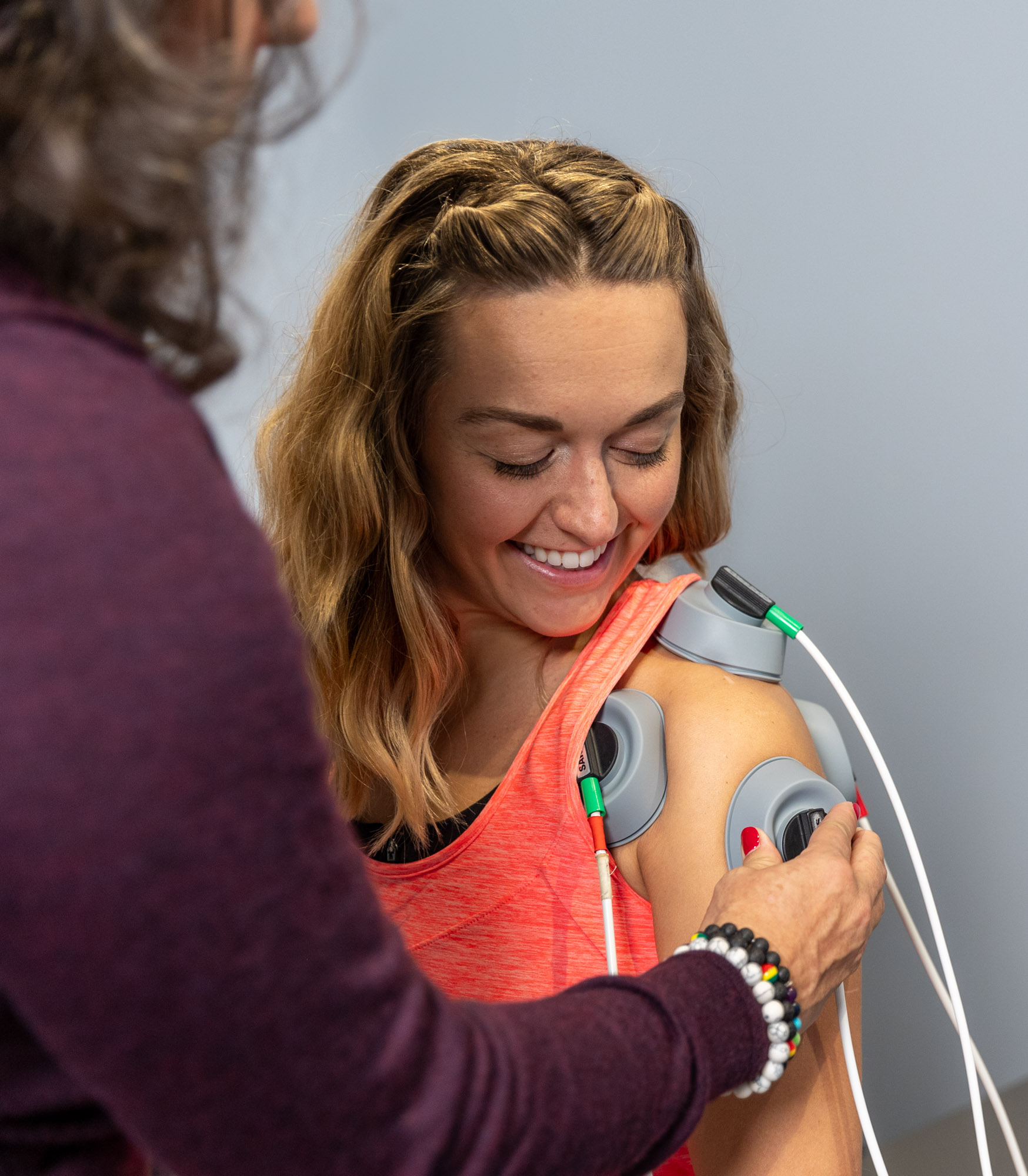 A female patient in a pink tank top has EMS applicators on her shoulder, a physcian providing sore rotator cuff treatment in Bucktown.