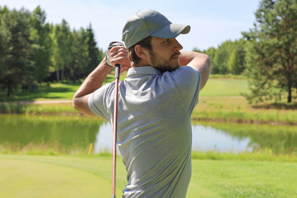 A young man having just completed a golf swing looks across the course, thinking of how he needs remedies for golfer’s elbow near Bucktown.