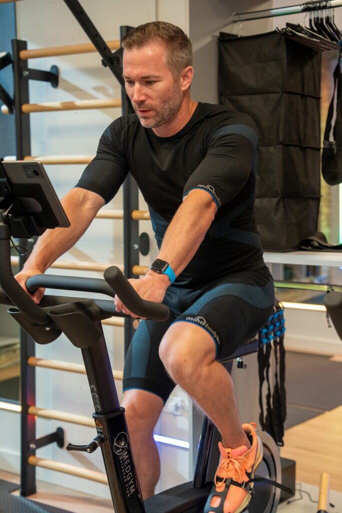 Man in a whole-body EMS suit riding the CAROL bike during a FastFit session